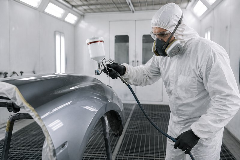 Opérateur en cabine de peinture carrosserie, combinaison intégrale et masque respiratoire